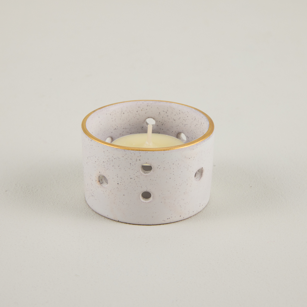 Speckled ceramic candle holder with a lit candle on a light gray background