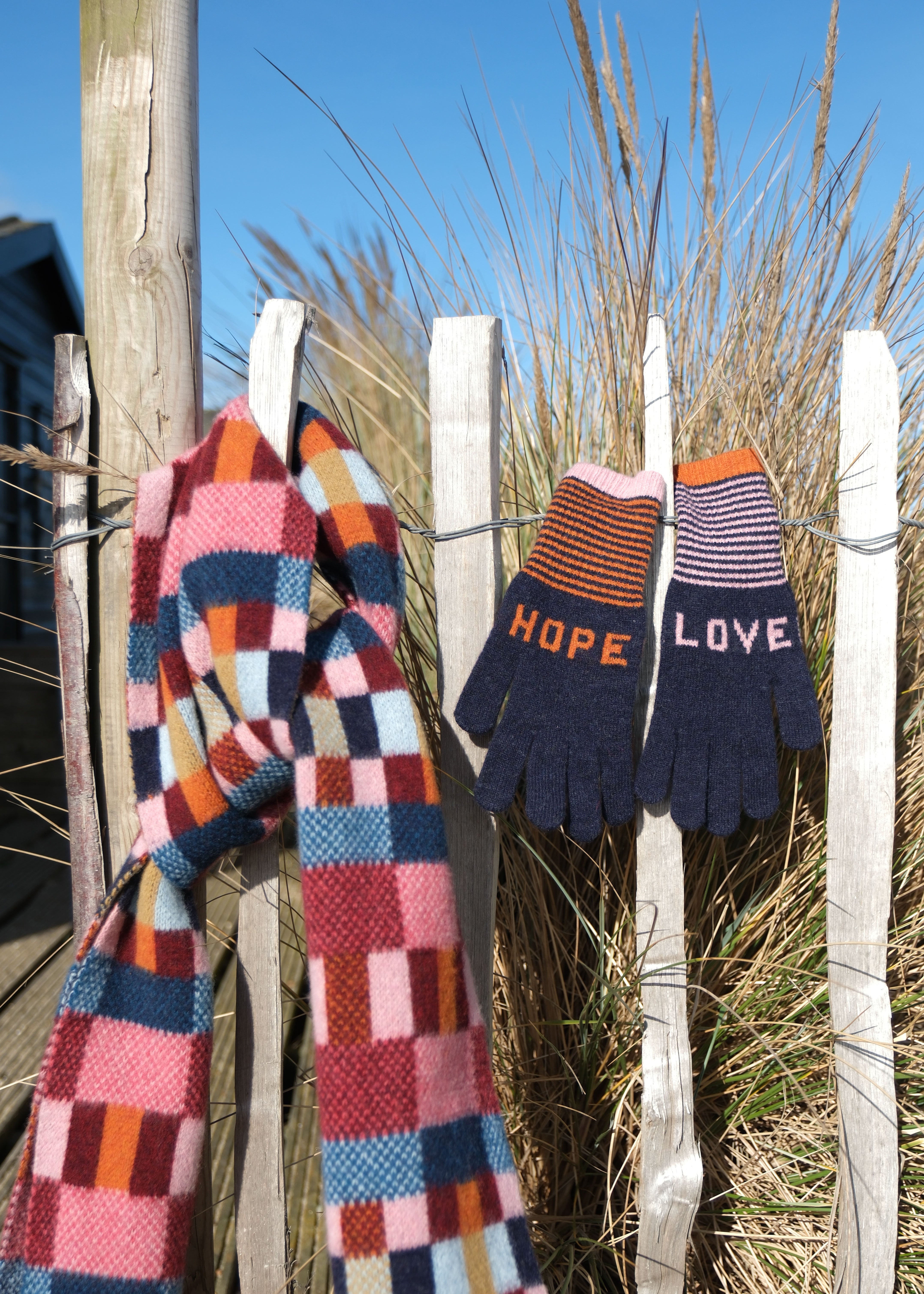 Colorful scarf and gloves with 'Hope' and 'Love' text hanging on a wooden fence.