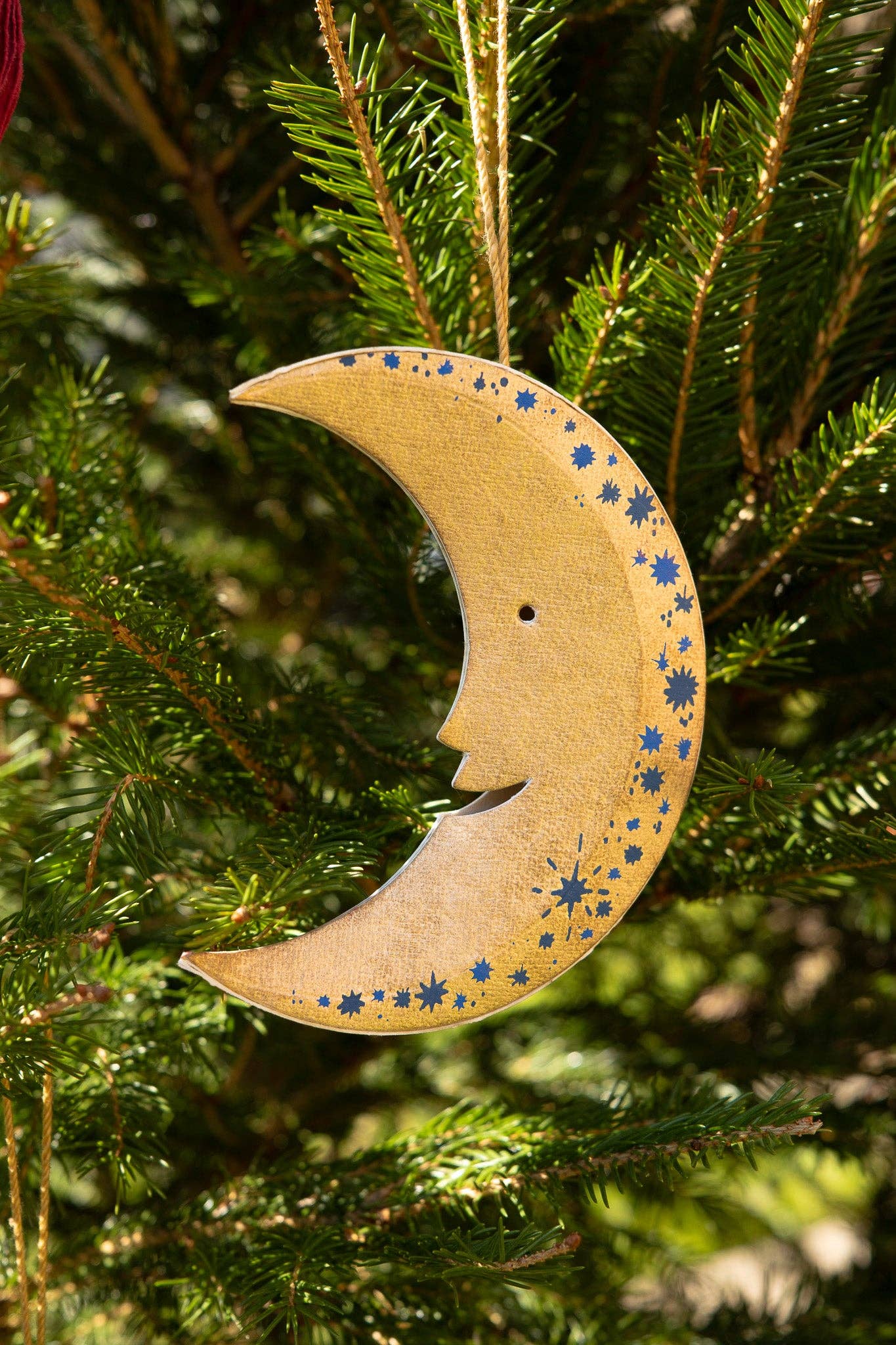 Wooden crescent moon ornament with blue star patterns hanging on a Christmas tree.