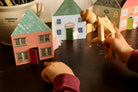 Children playing with wooden toy figures and paper house models on a table.
