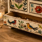 Decorative jewelry box with floral and bird designs on a wooden surface.