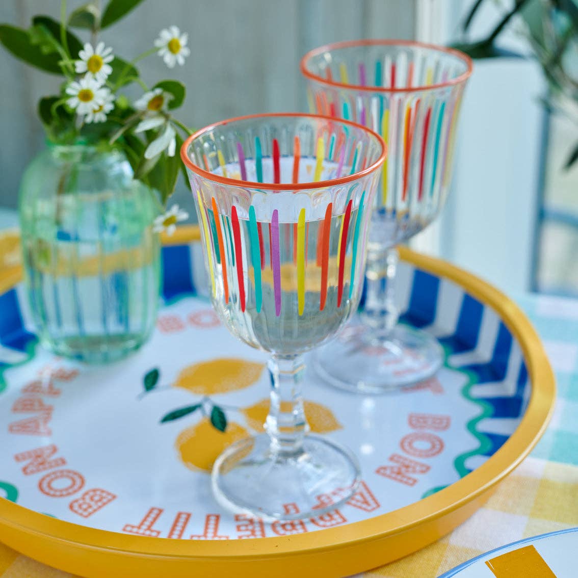 Colorful striped glasses on a decorative tray with a floral arrangement in the background.