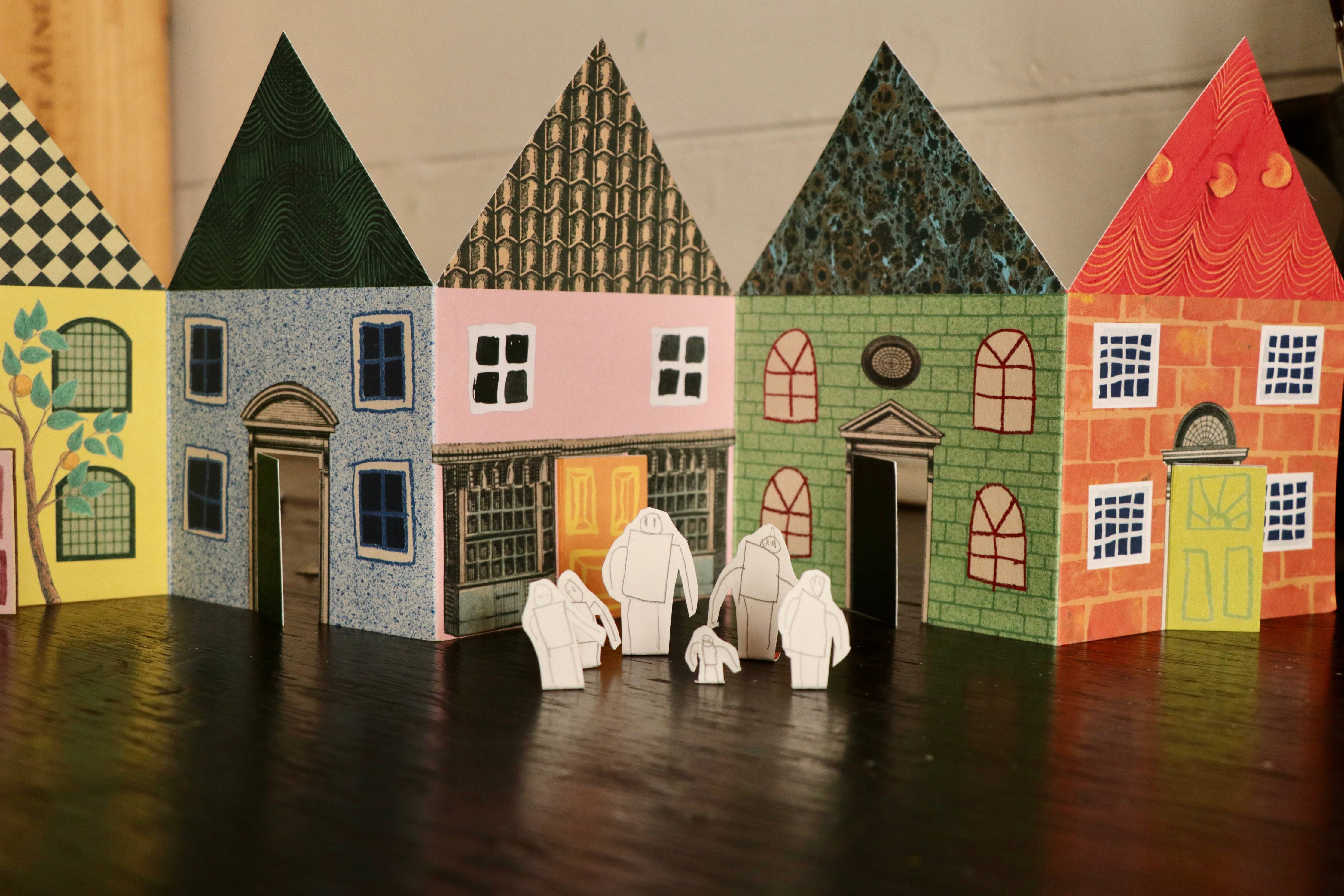 Model of a small town with colorful houses and white figures on a dark surface.