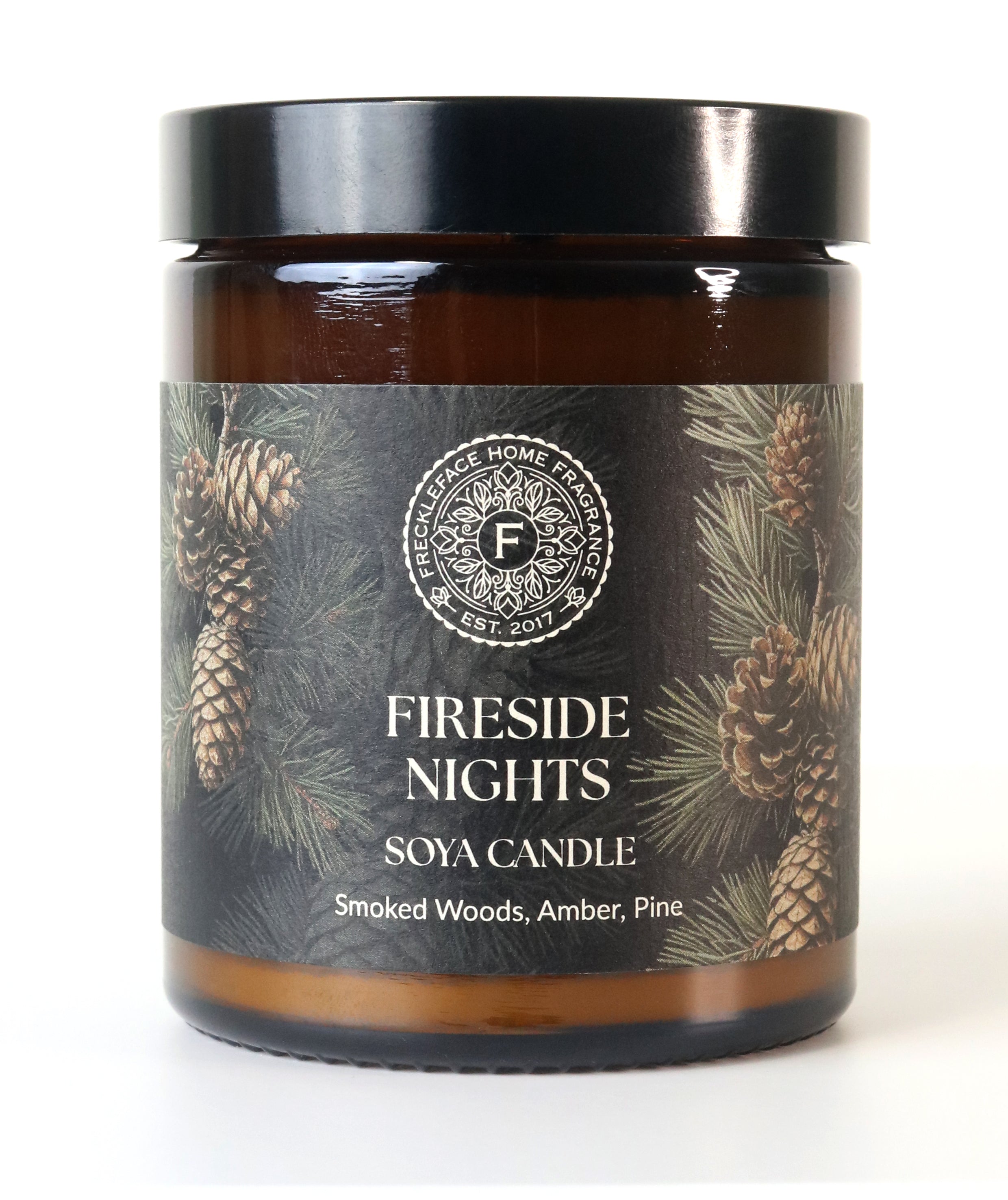 Candle labeled 'Fireside Nights' with pine cone design on a white background