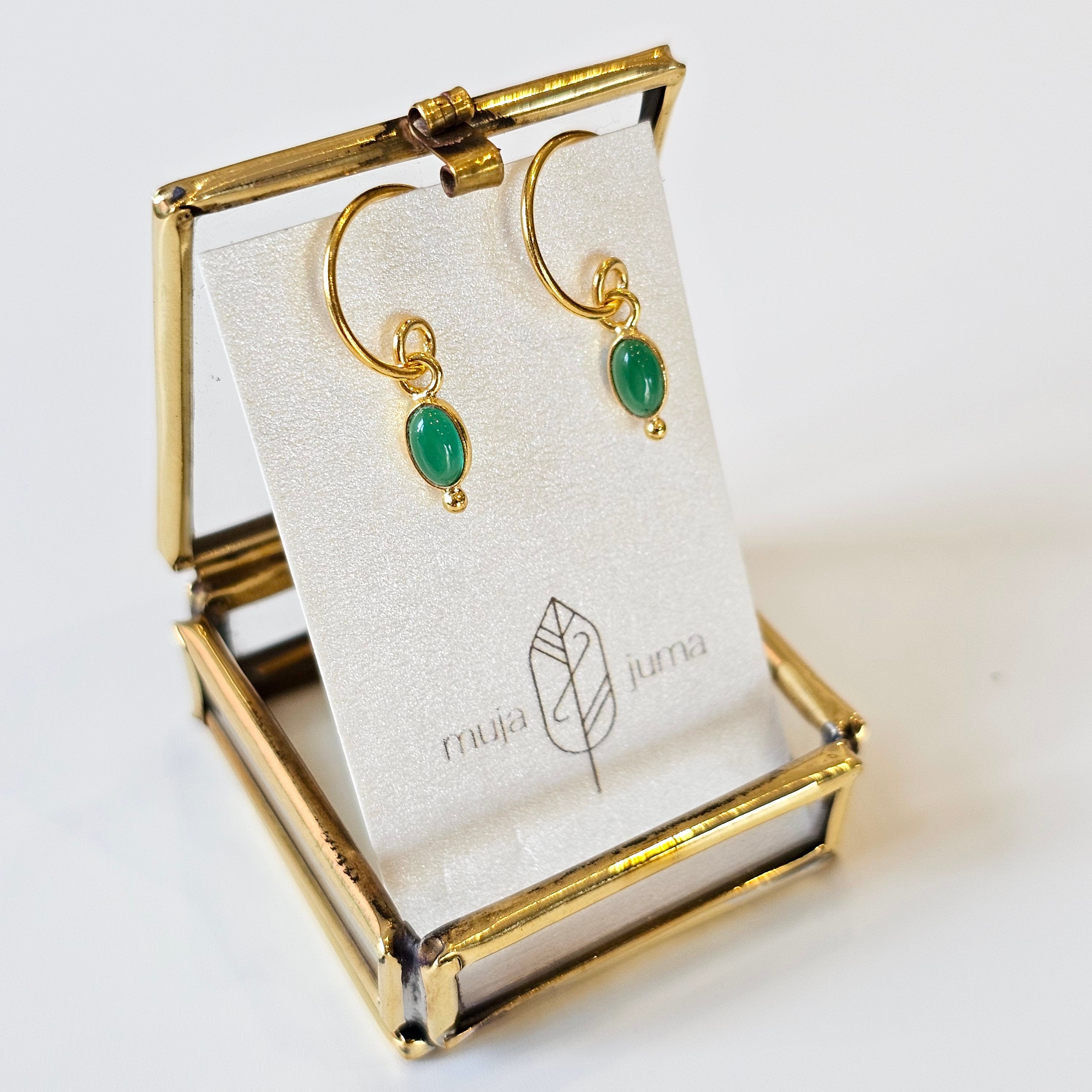 Gold hoop earrings with green stones on a branded card in a gold stand.