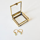 Gold earring box with gold earrings featuring light blue-green stones on a white background