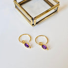 Gold hoop earrings with amethyst gemstones on a white background