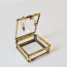 Gold jewellery box with amethyst earrings on a white background