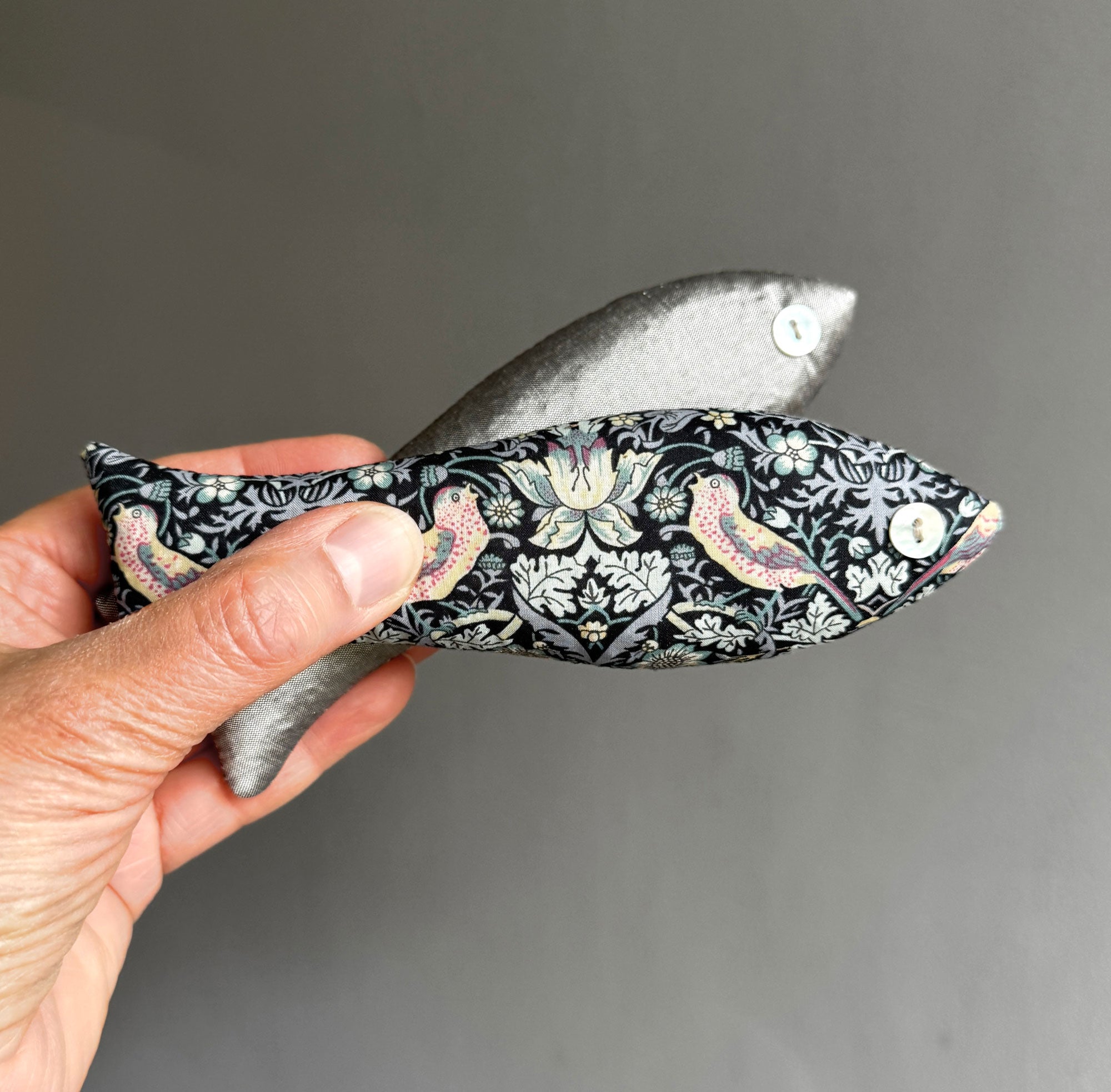 Hand holding a decorative sachet with Strawberry Thief pattern against a grey background