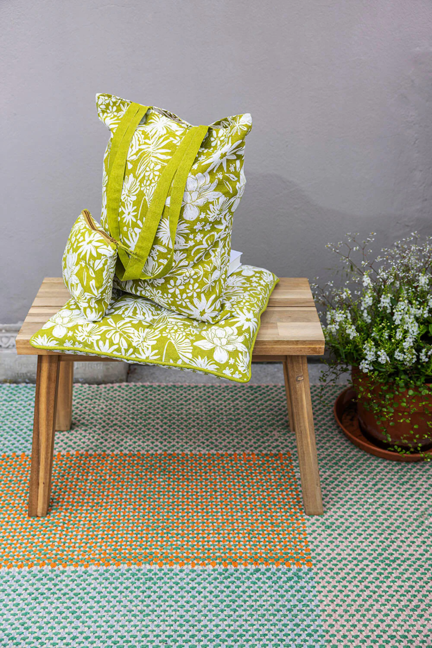 Green floral bag on a wooden chair with a grey wall and plant in the background