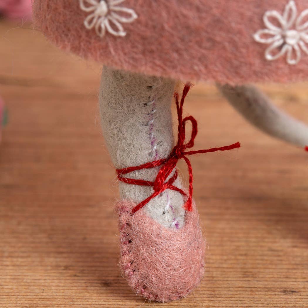 Detail showing a pink ballet shoe with red tie worn on a milky white mouse leg. 