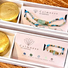 Gemstone and gold vermeil beaded bracelet and ring and gold travel tins in white presentation boxes on wooden surface.