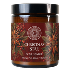 A soy candle in an amber glass jar with a black lid and a dark red holiday label featuring star anise, pine needles, and berries. The label reads 'CHRISTMAS STAR' and 'SOYA CANDLE' with 'Orange Peel, Clove, Fir Balsam' below.