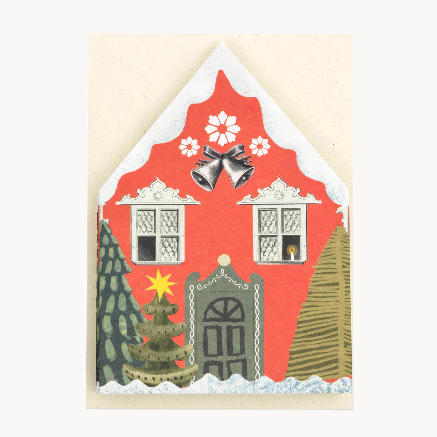 A festive Christmas house card with a red facade, white snow-dusted roof and trim, two windows, silver bells, white flowers, a grey door, and two green trees on a cream background. Shown folded flat to fit the off white envelope.