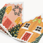 A close-up of a folded card featuring a whimsical winter house illustration with a wreath, Christmas tree, and colourful windows on a white background.