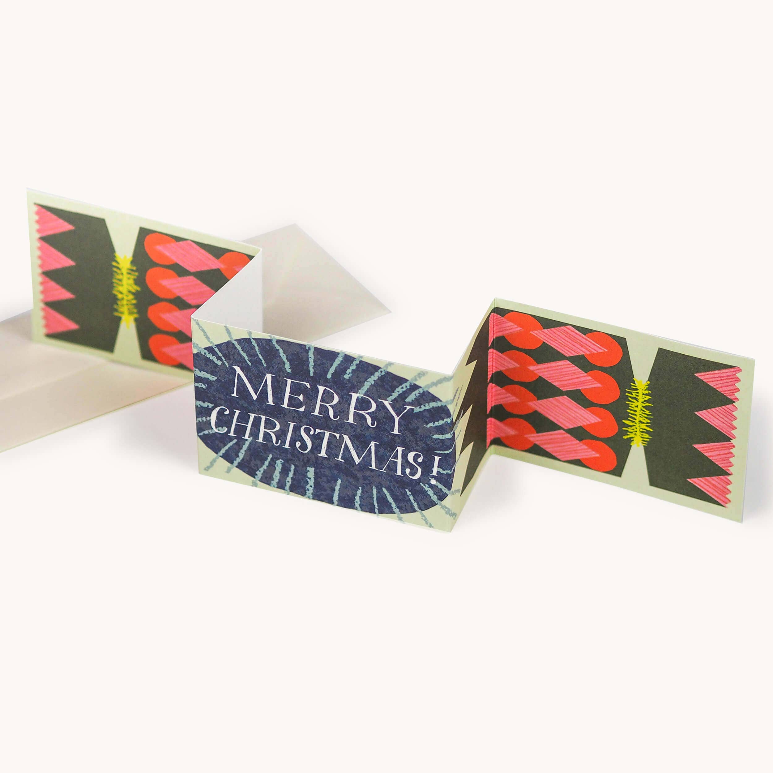 A folded Christmas greeting card with a cracker design, featuring the text 'MERRY CHRISTMAS' on a dark blue oval panel, flanked by red and pink abstract patterns.