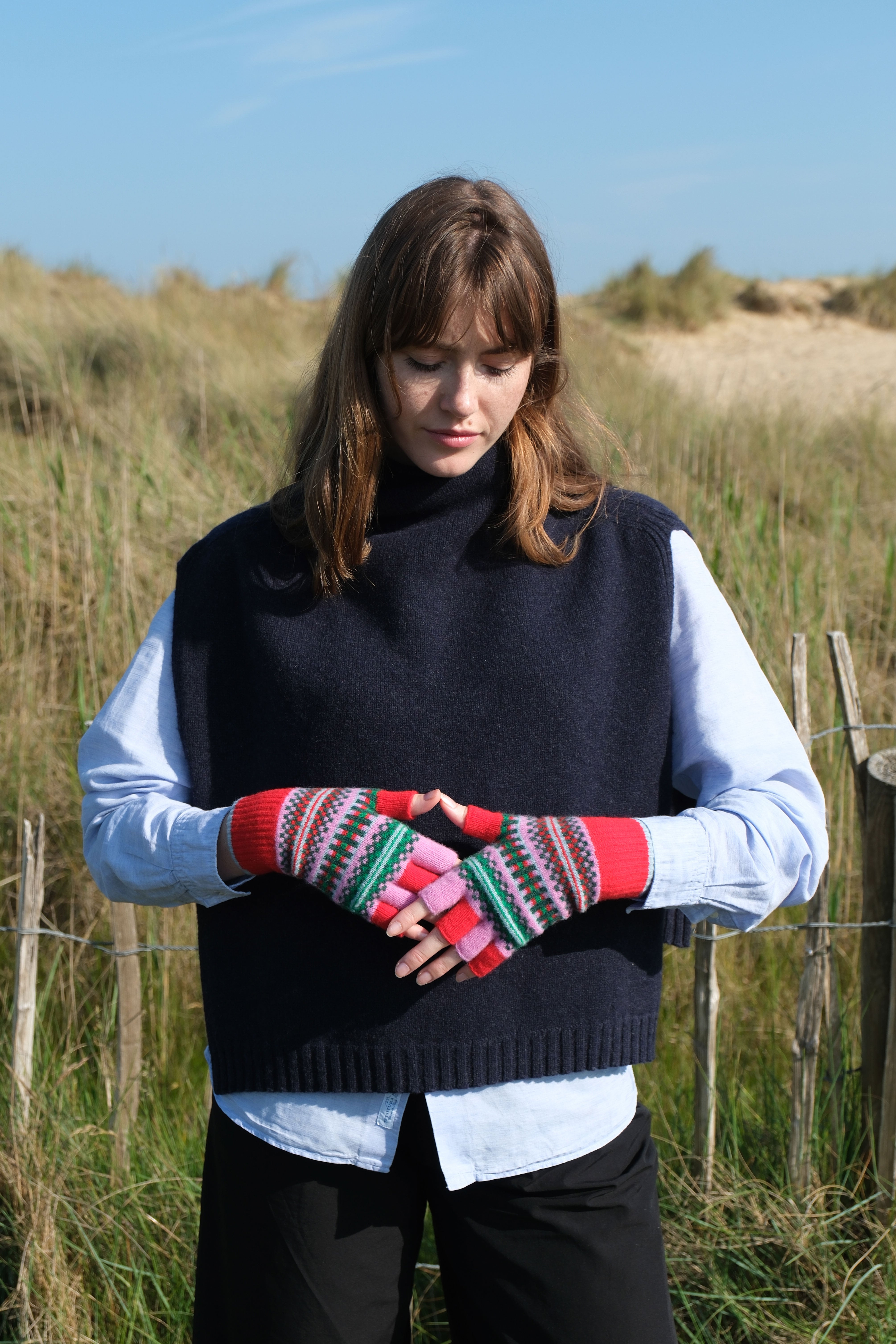 Woman wearing a black sleeveless sweater and colorful fingerless gloves in a field.
