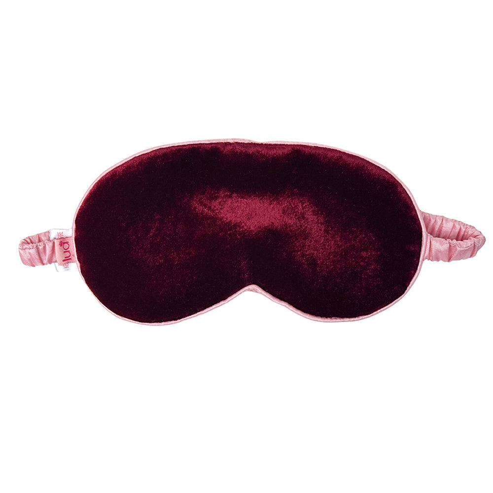 A plush velvet sleep mask in deep burgundy with a light pink elastic strap, shown against a plain white background.