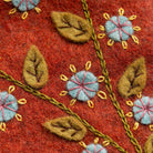 Detail of colourful red felt and botanical embroidery in blue, yellow, green and pink with olive green felt leaves and blue flower designs. 