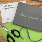 Grey box with 'lime tree design' branding, scissors, and green fabric on a wooden surface.