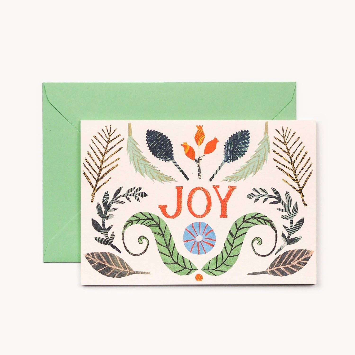 A greeting card with botanical illustrations, shown with a green envelope behind it on a light background. The card features the word 'JOY' in red letters with green leaves, red-orange berries, and a blue-and-orange sun motif.