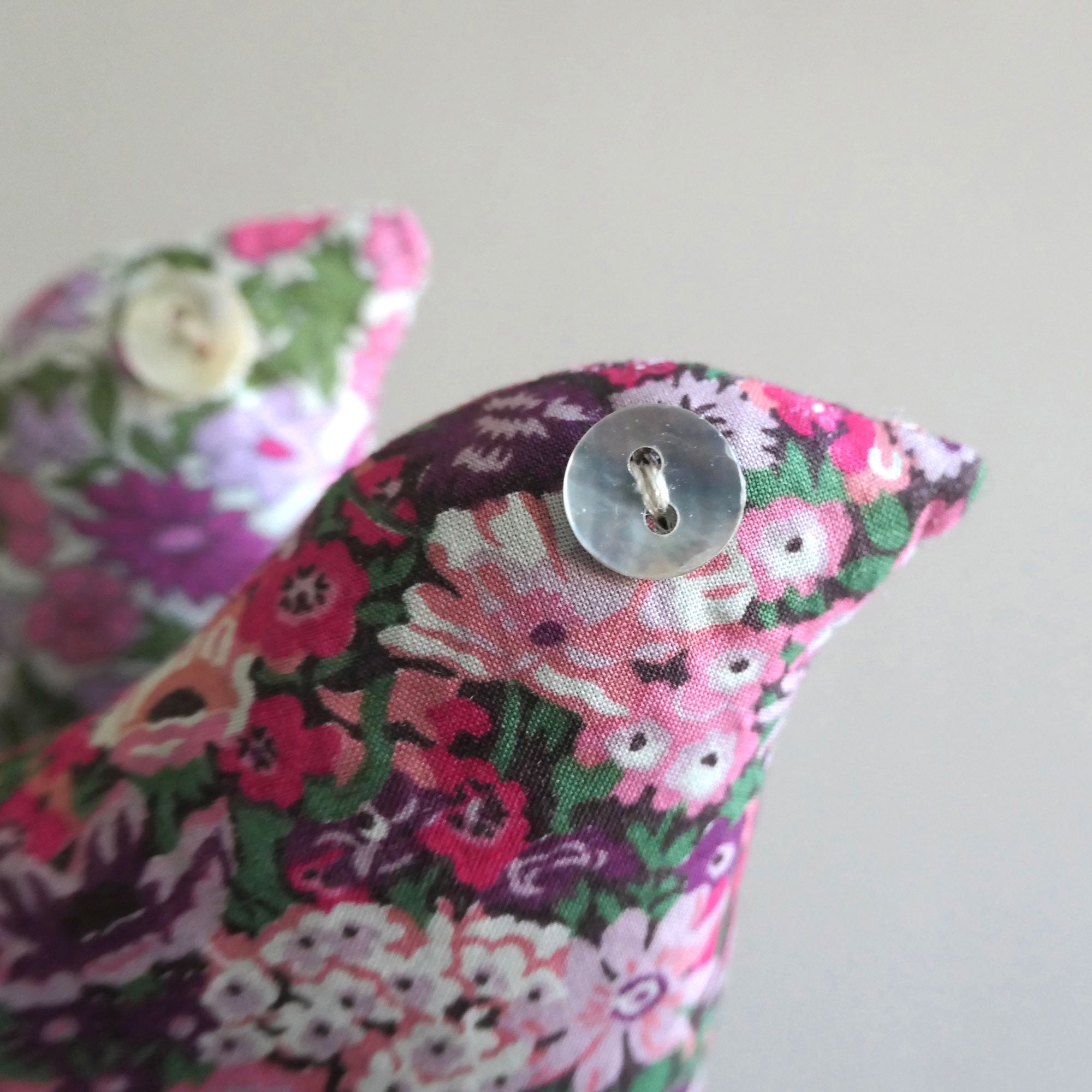 Floral fabric bird-shaped lavender sachet with a button on a light grey background
