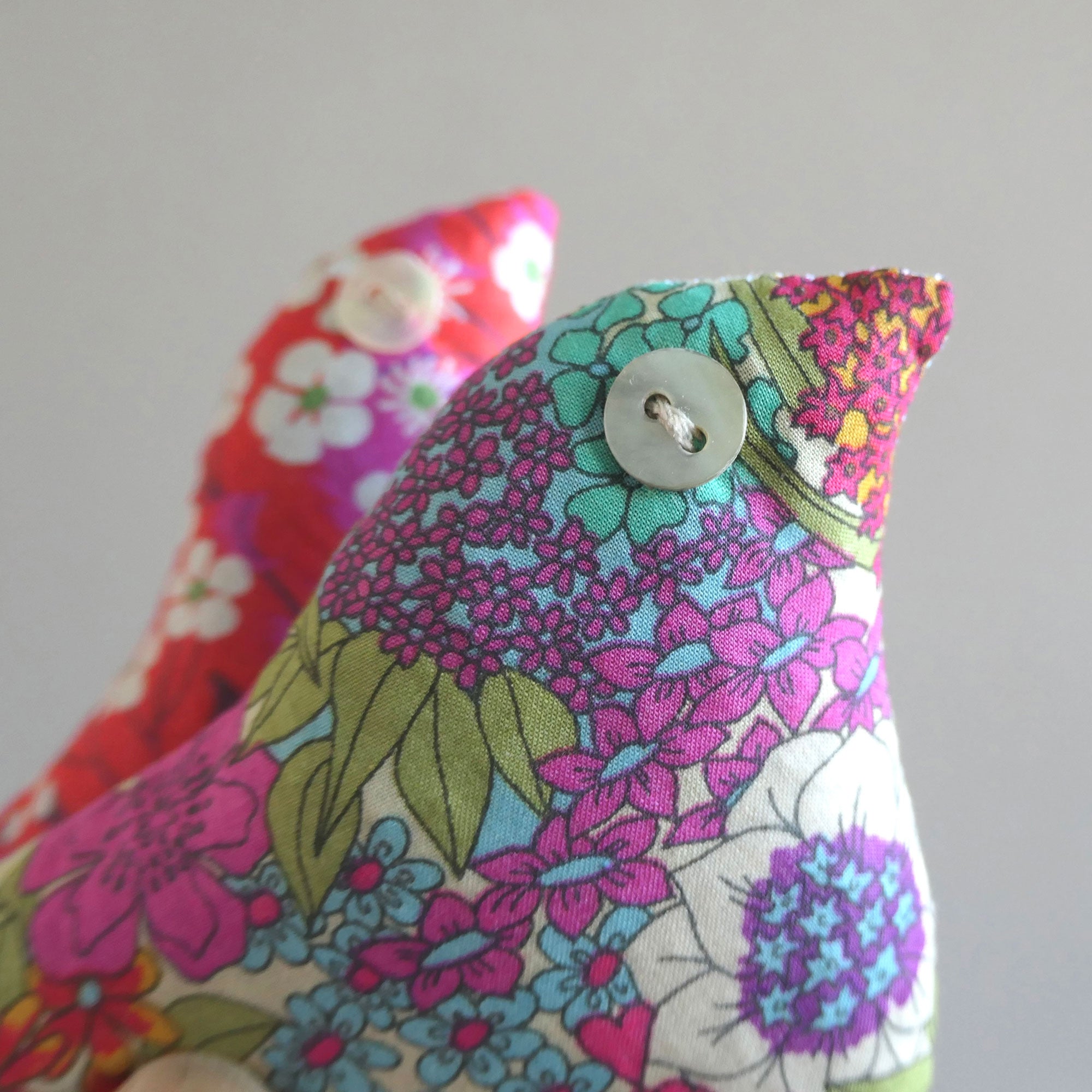 Floral-patterned fabric bird sachet with a button on a grey background