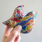 Colourful floral-patterned bird-shaped lavender sachets held by a hand against a plain background