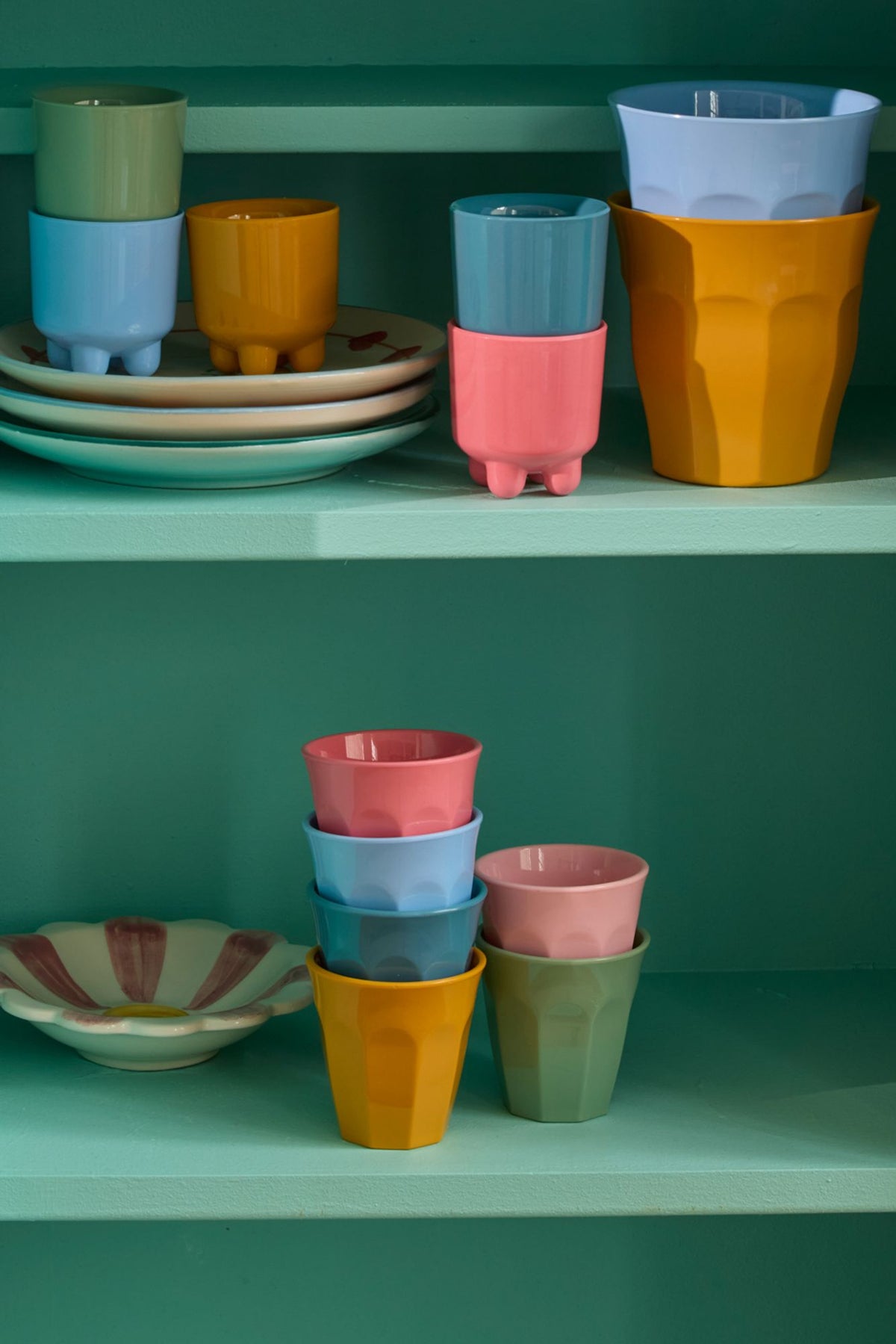 Colorful ceramic cups and bowls on a green shelf