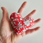 Hand holding a red heart-shaped fabric with white floral pattern on a light background