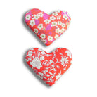 Two heart-shaped cushions with pink and red floral patterns on a white background