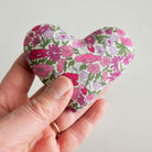 Hand holding a floral-patterned heart-shaped object against a plain background