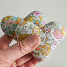 Hand holding a floral-patterned heart-shaped fabric item against a plain background