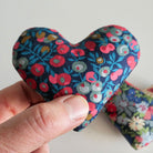 Hand holding a floral-patterned heart-shaped fabric item against a white background