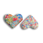 Two heart-shaped red cushions with red, yellow and blue floral patterns on a white background
