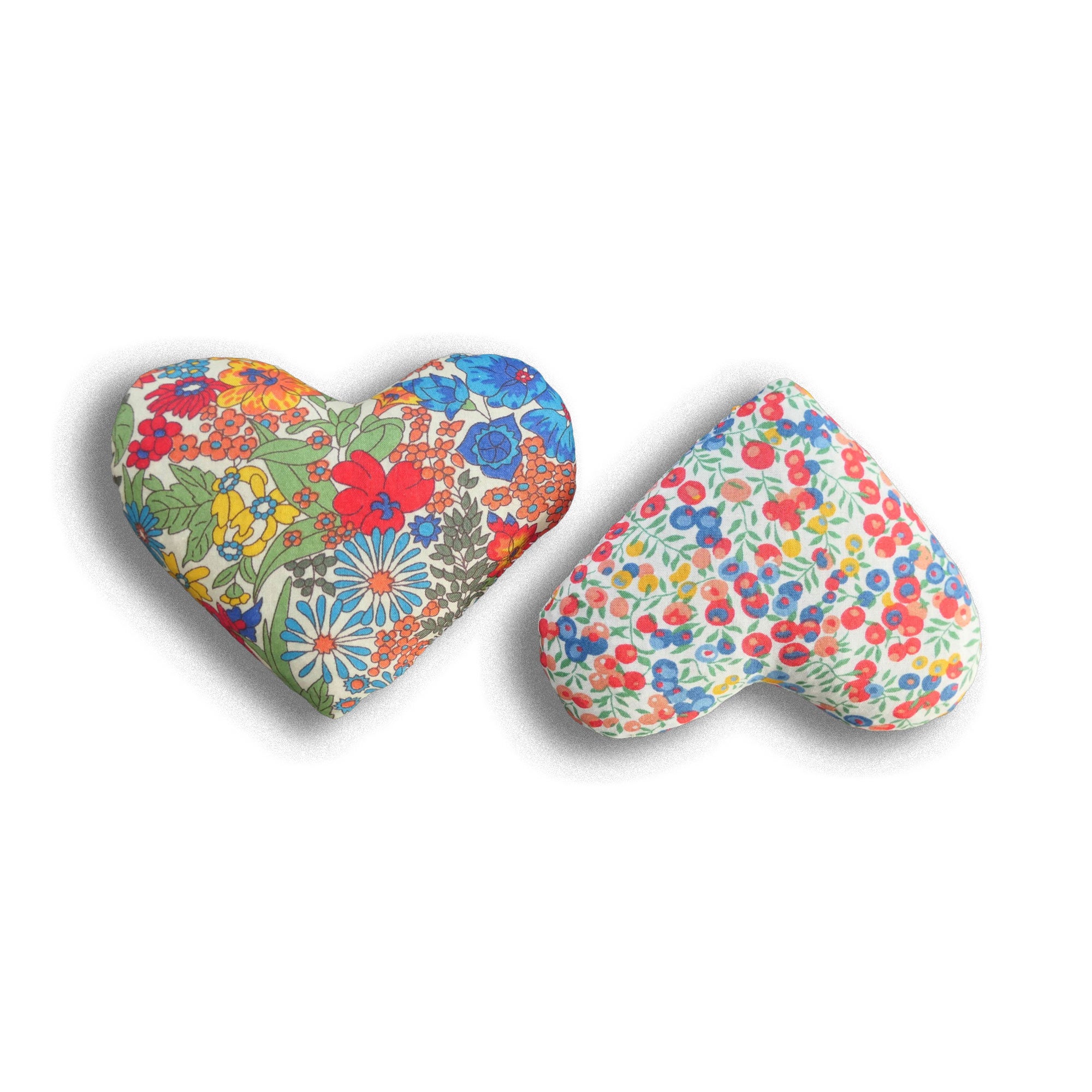 Two heart-shaped red cushions with red, yellow and blue floral patterns on a white background