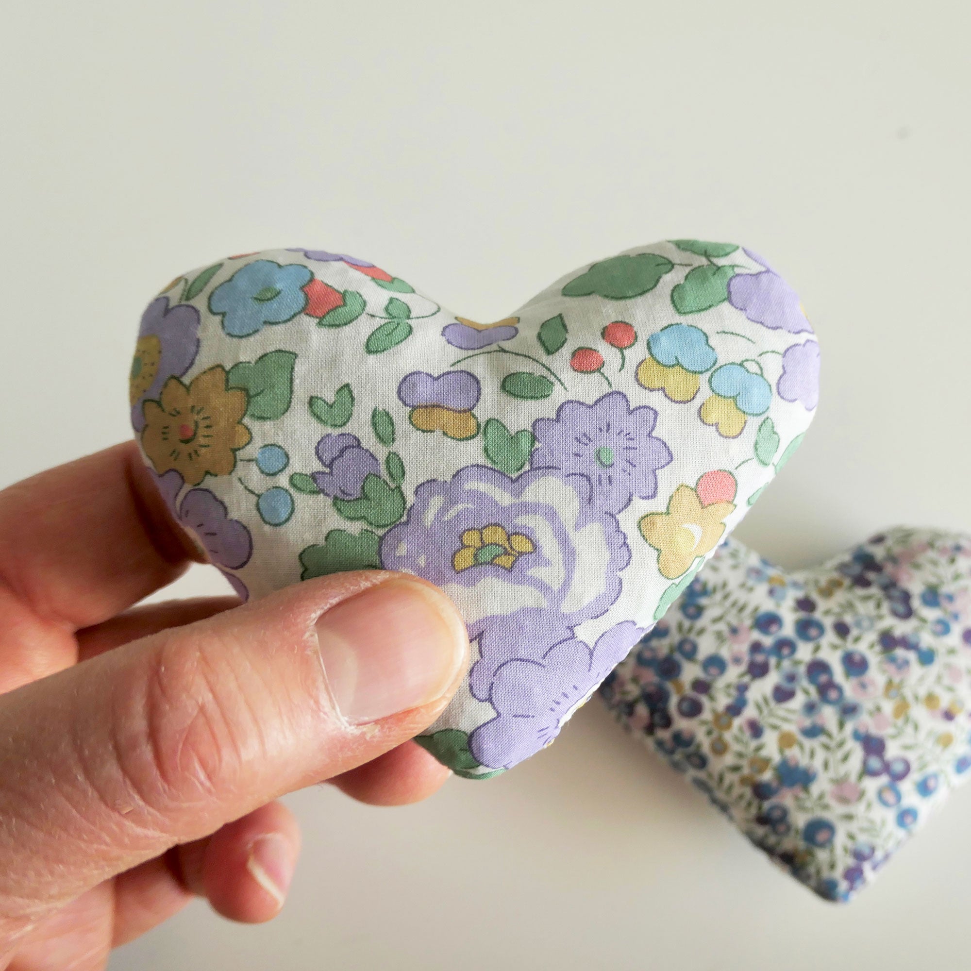 Hand holding a floral-patterned heart-shaped fabric item against a plain background