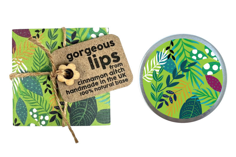Lip balm  with a decorative label and a small round container with a green leaf design on a white background.