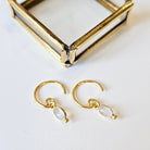 Gold hoop earrings with moonstone drops on a white surface