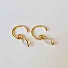 Gold hoop earrings with moonstone drops on a light gray background