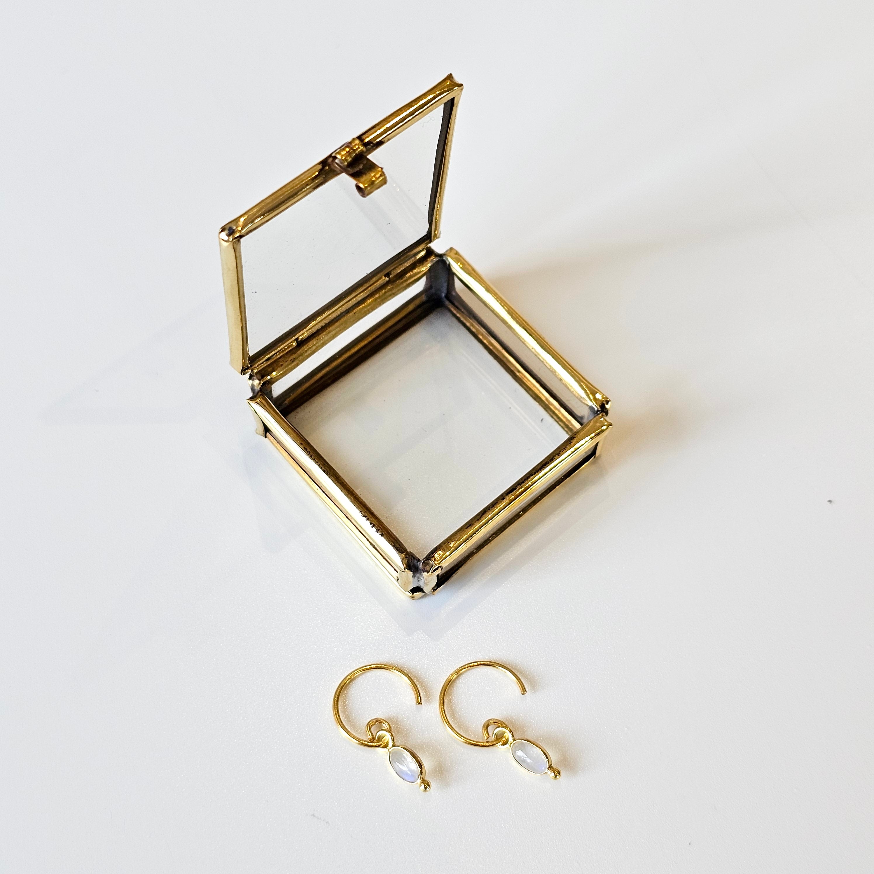 Gold jewelry box with open lid on a white background, featuring gold earrings.