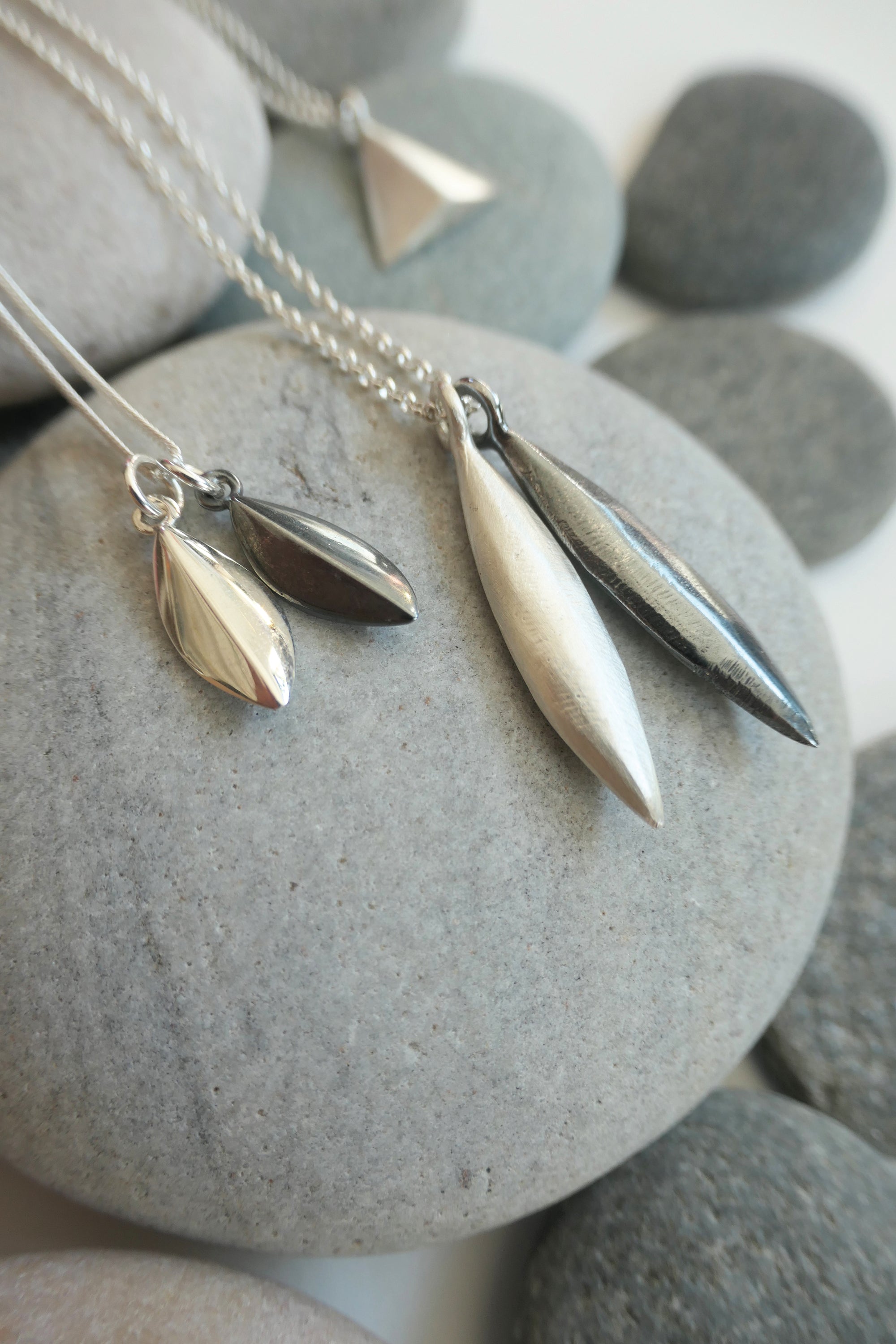 Silver seed shaped pendants on a chain against a stone background