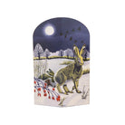 A decorative arched card featuring an illustrated winter landscape with a hare in the snow under a full moon, displayed on a light wood surface against a warm beige background.