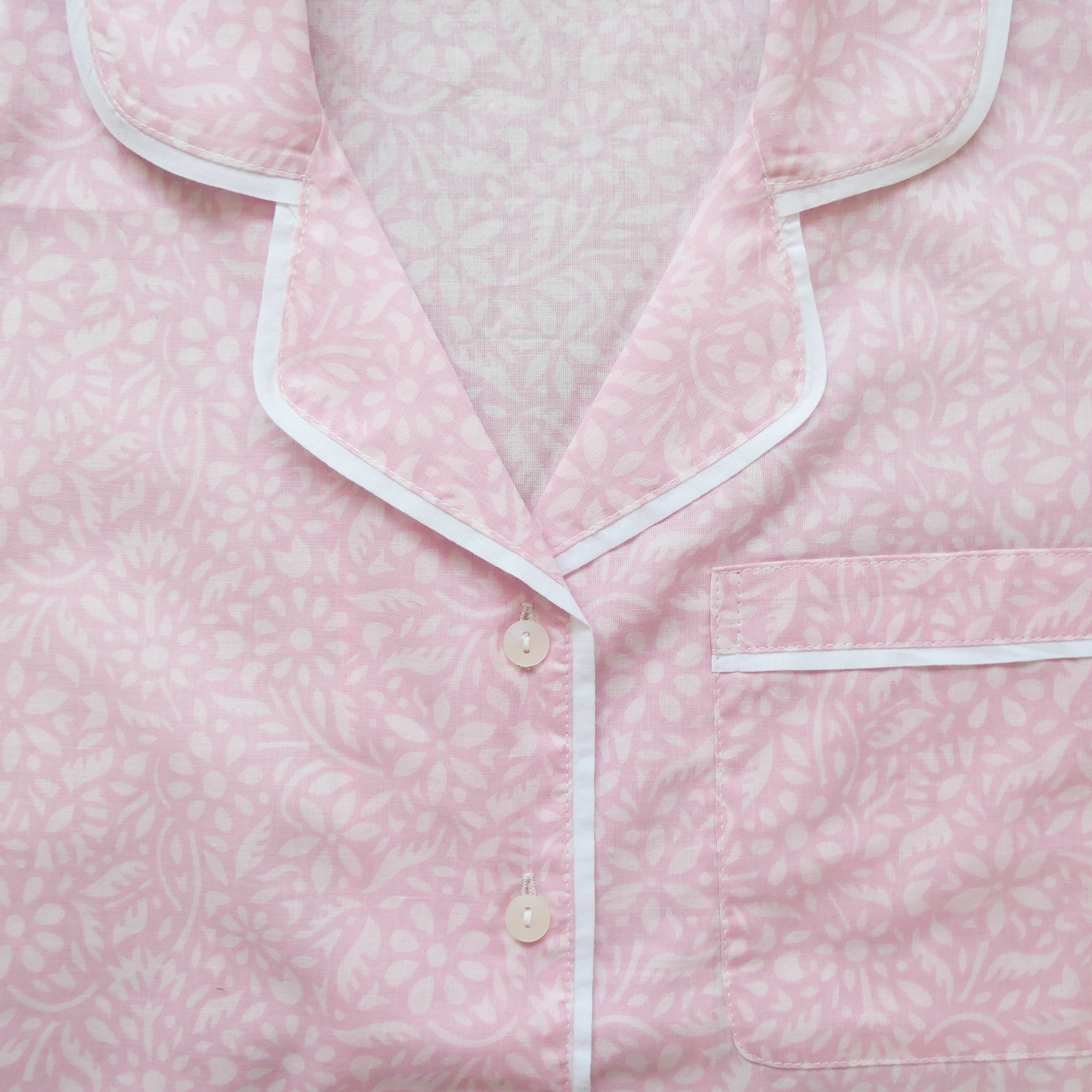 Pink pajama top with white trim on a light pink background