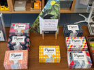 Collection of Pigeon product boxes on a wooden surface with a colourful poster in the background.