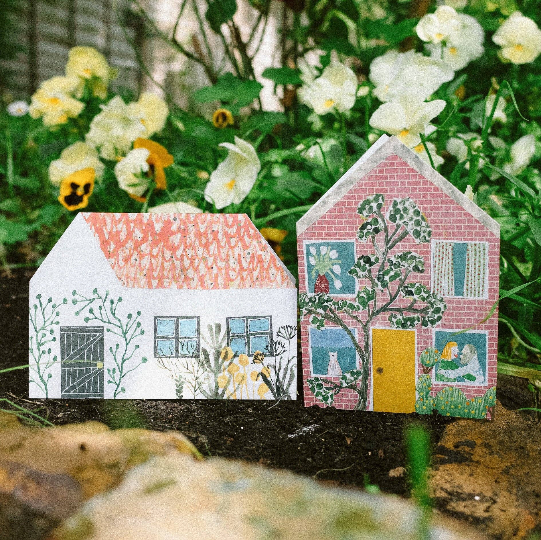 Two house themed cards with colourful designs on a natural background with flowers.
