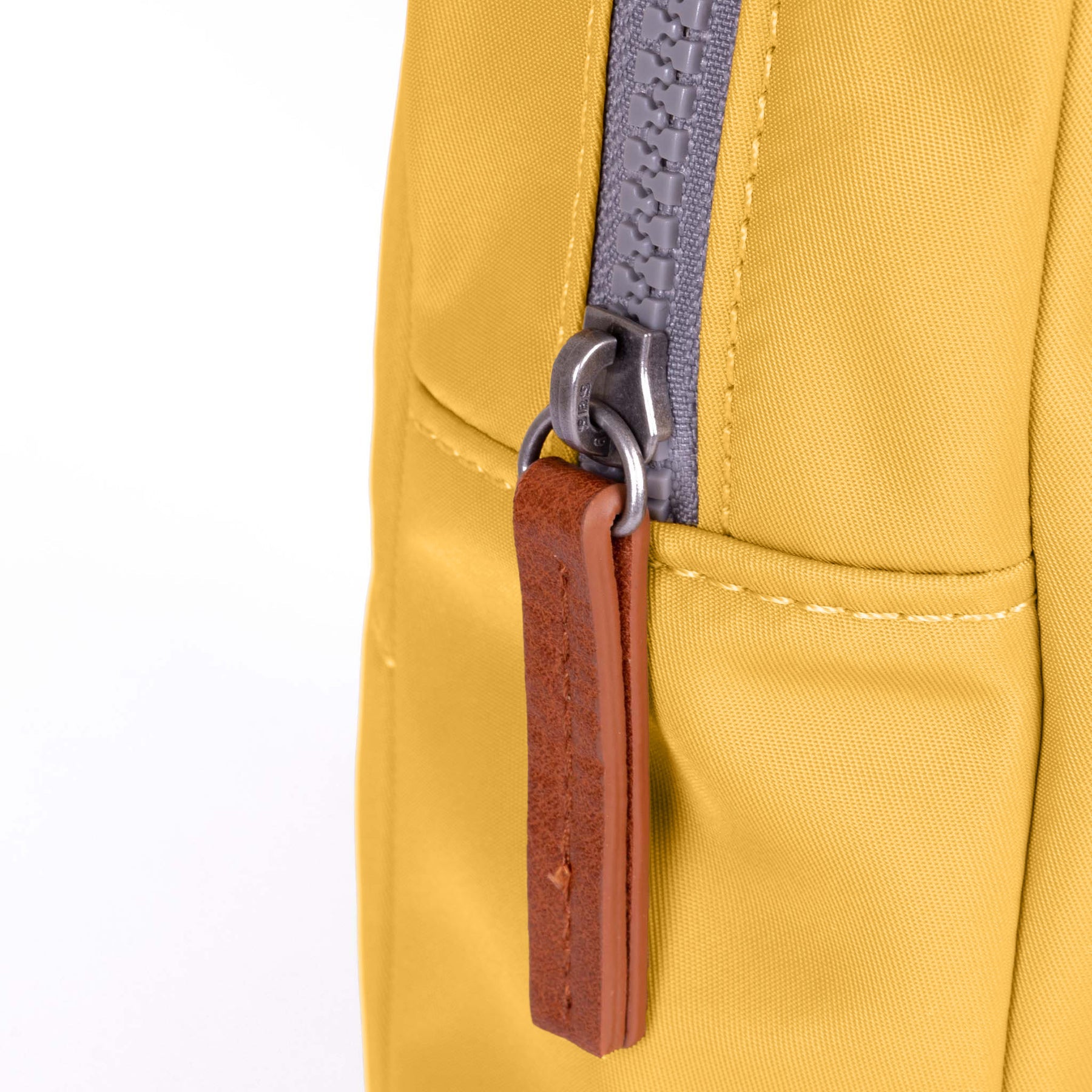 Close-up of a yellow backpack with a brown leather tag and gray zipper.