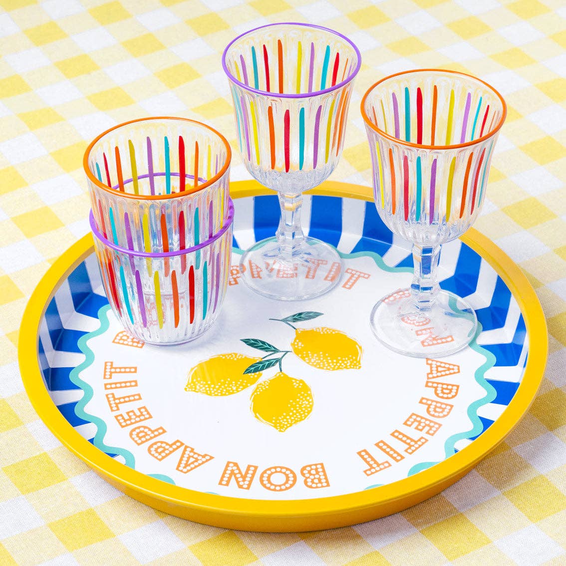 Colorful striped glasses on a decorative plate with lemon design on a checkered tablecloth.