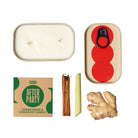 Candle, cinnamon stick, ginger root, and branded packaging on a white background