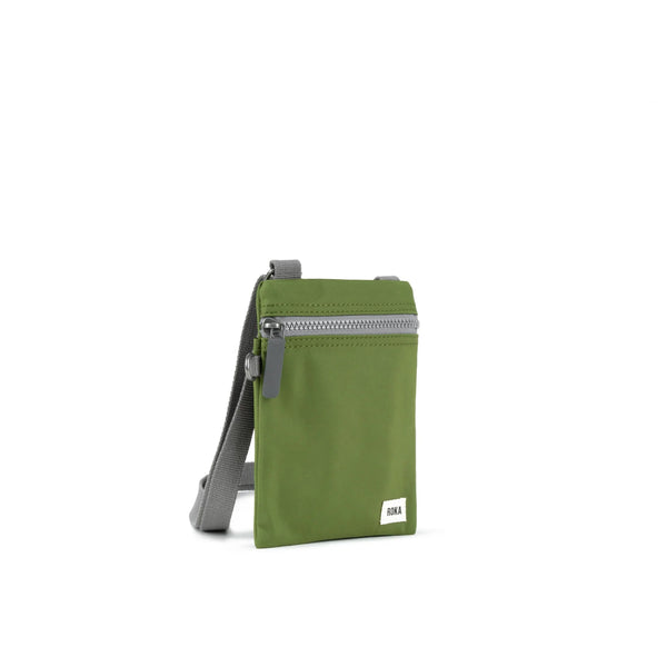 A photo of the front and side of a small rectangular avocado green pocket bag. It has a grey zip horizontally at the top, grey straps, and a small ROKA logo in the bottom right corner. 